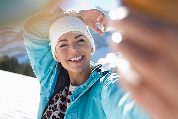 Femme qui se prend en selfie à la montagne, avec une veste de ski bleue et un pull à motifs léopard
