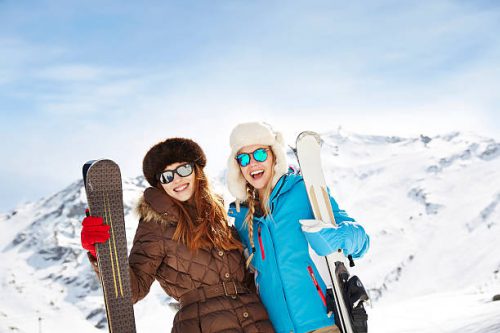 Deux jeunes femmes en combinaison qui portent des skis à la montagne