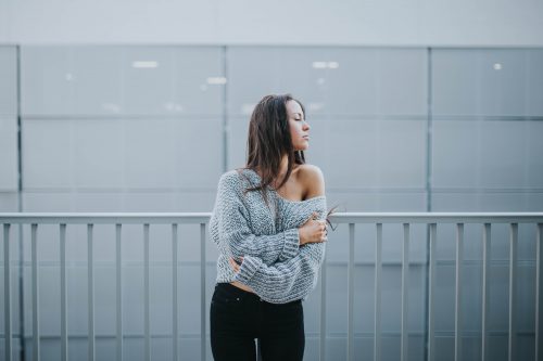 femme brune portant un pull gris tombé sur une épaule et un pantalon noir